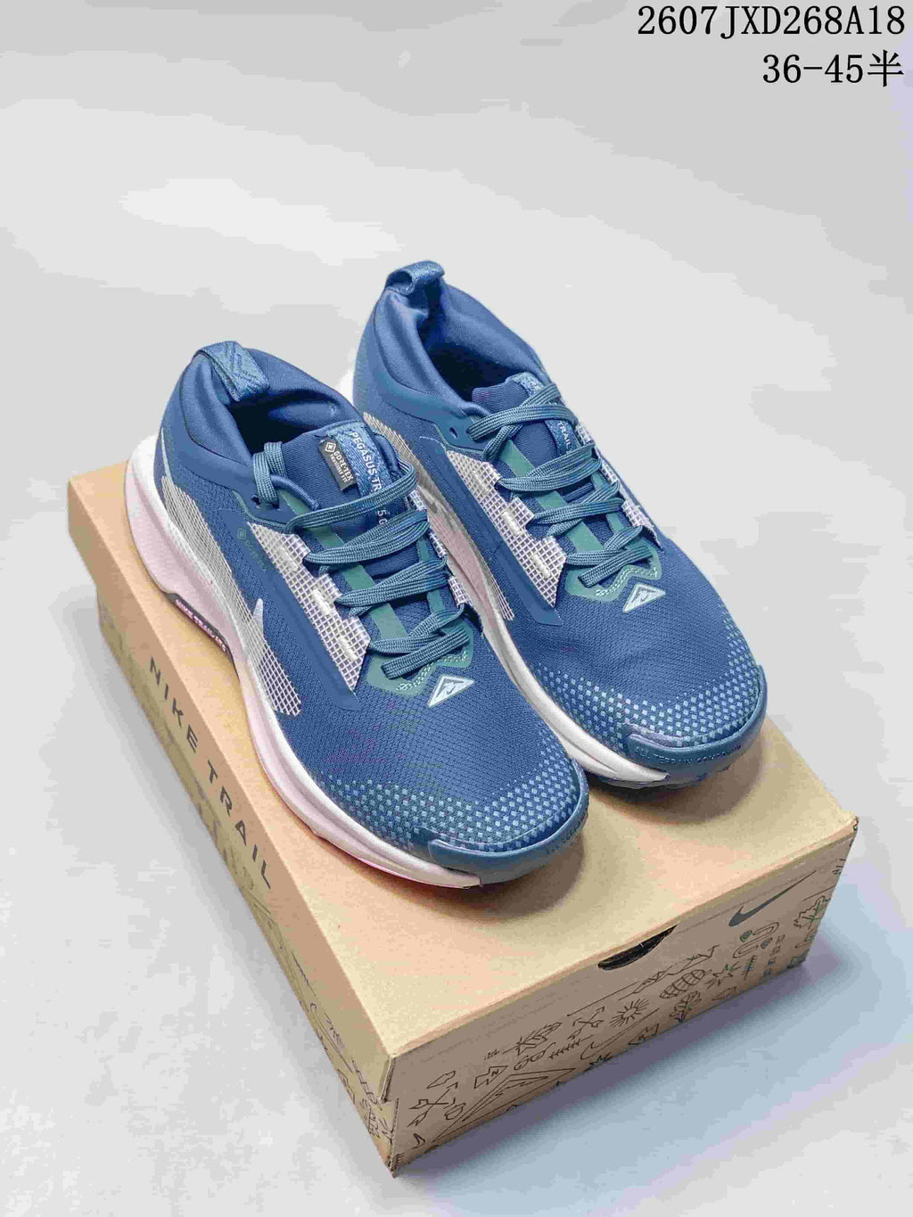 Pair of blue Nike Pegasus Trail 5 sneakers displayed on a shoebox, with the style code and size range visible at the top.