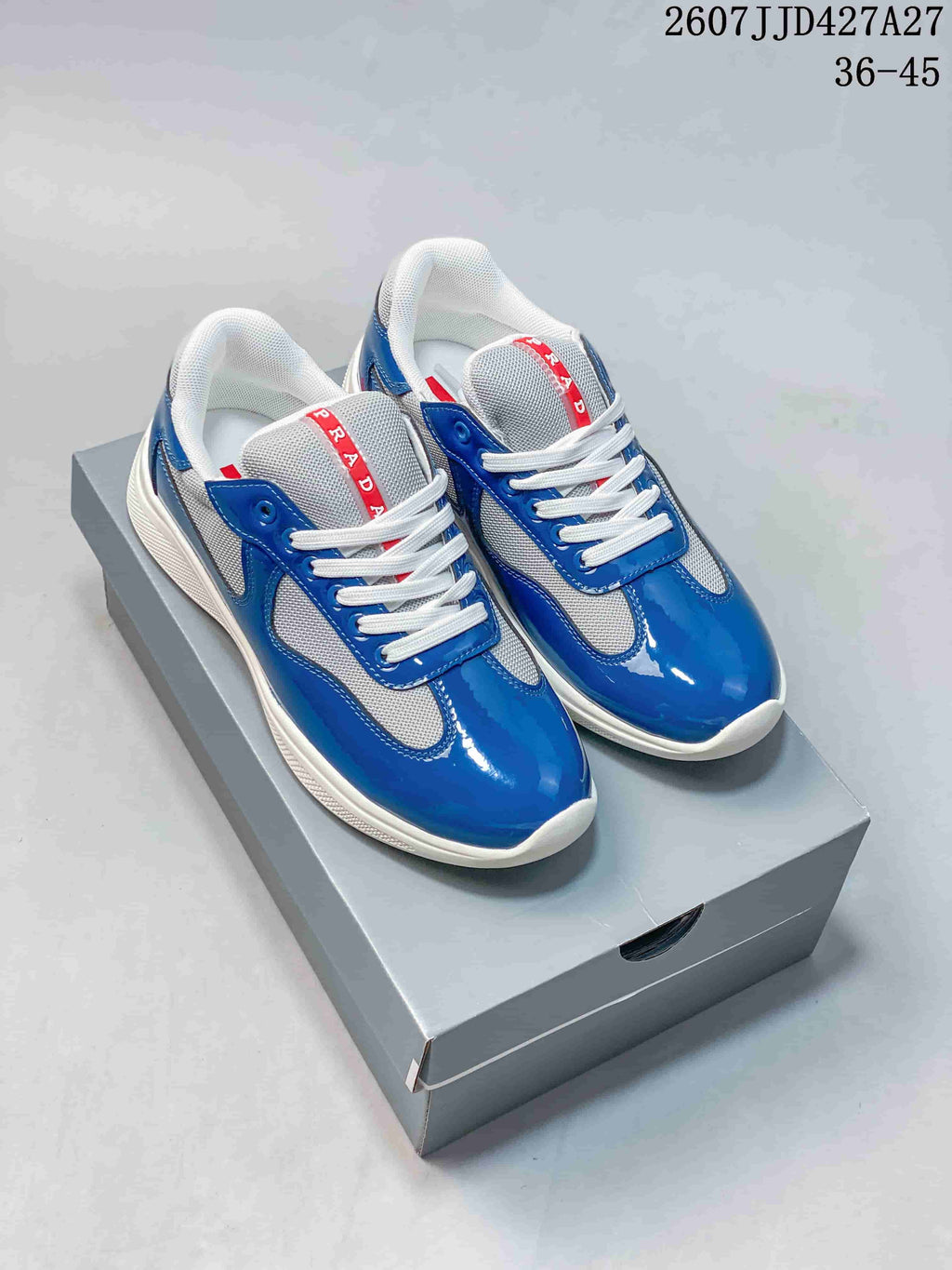 Pair of blue and white Prada America's Cup low-top sneakers displayed on a gray shoebox.