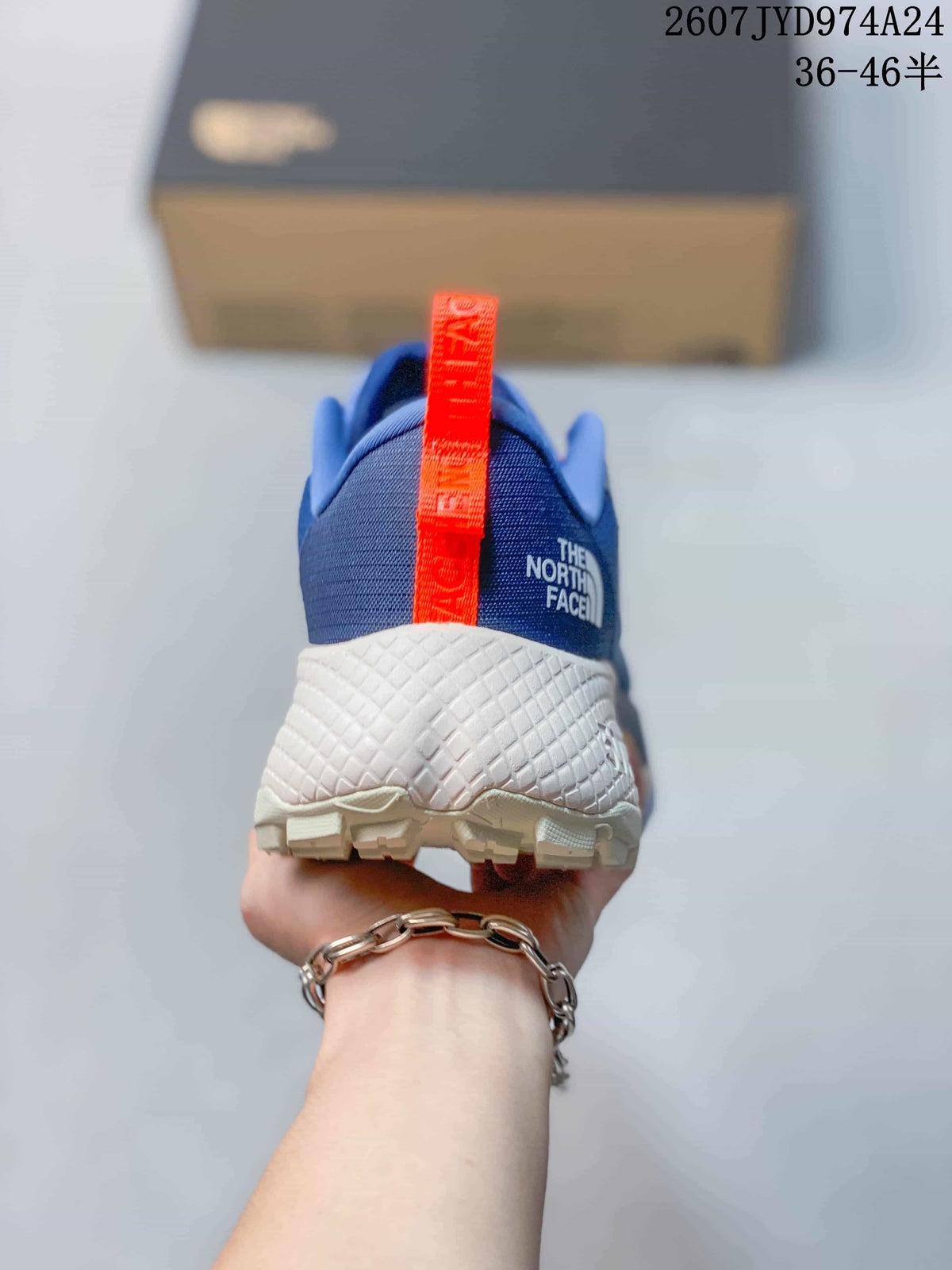 Rear view showing the blue heel, orange pull tab, The North Face branding, and textured white midsole.