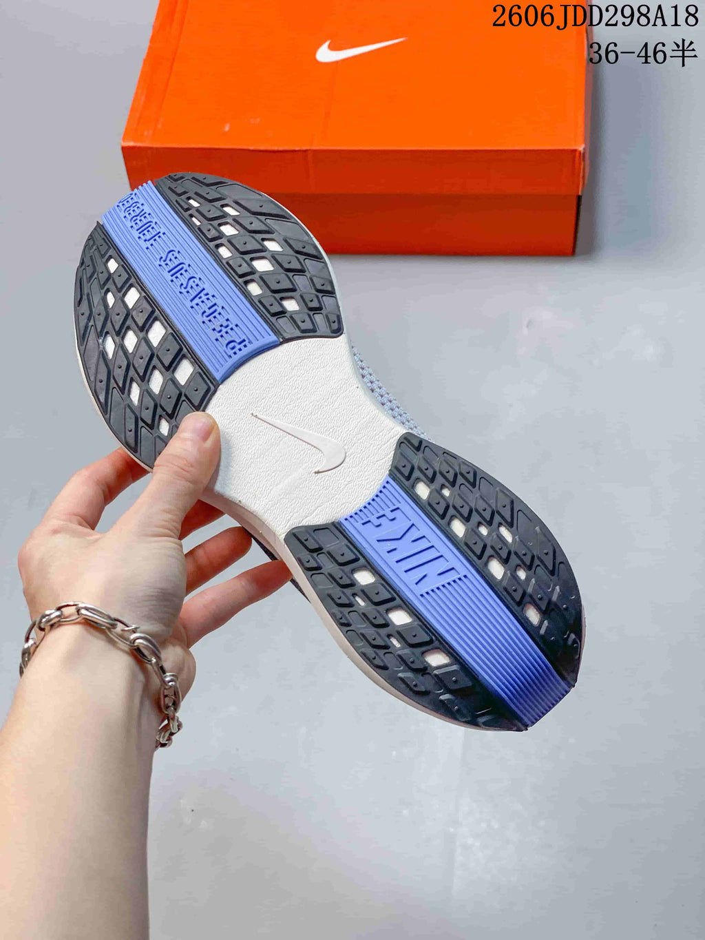 Close view of the patterned black, white and blue rubber outsole of the Nike running shoe beside an orange shoebox.