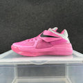 Side view of a pink Nike basketball sneaker with a black Swoosh strap, mesh panels, and a light-colored heel section.