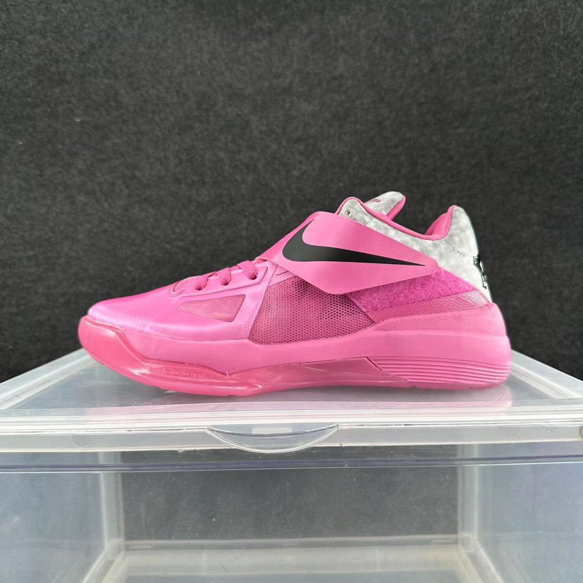 Side view of a pink Nike basketball sneaker with a black Swoosh strap, mesh panels, and a light-colored heel section.