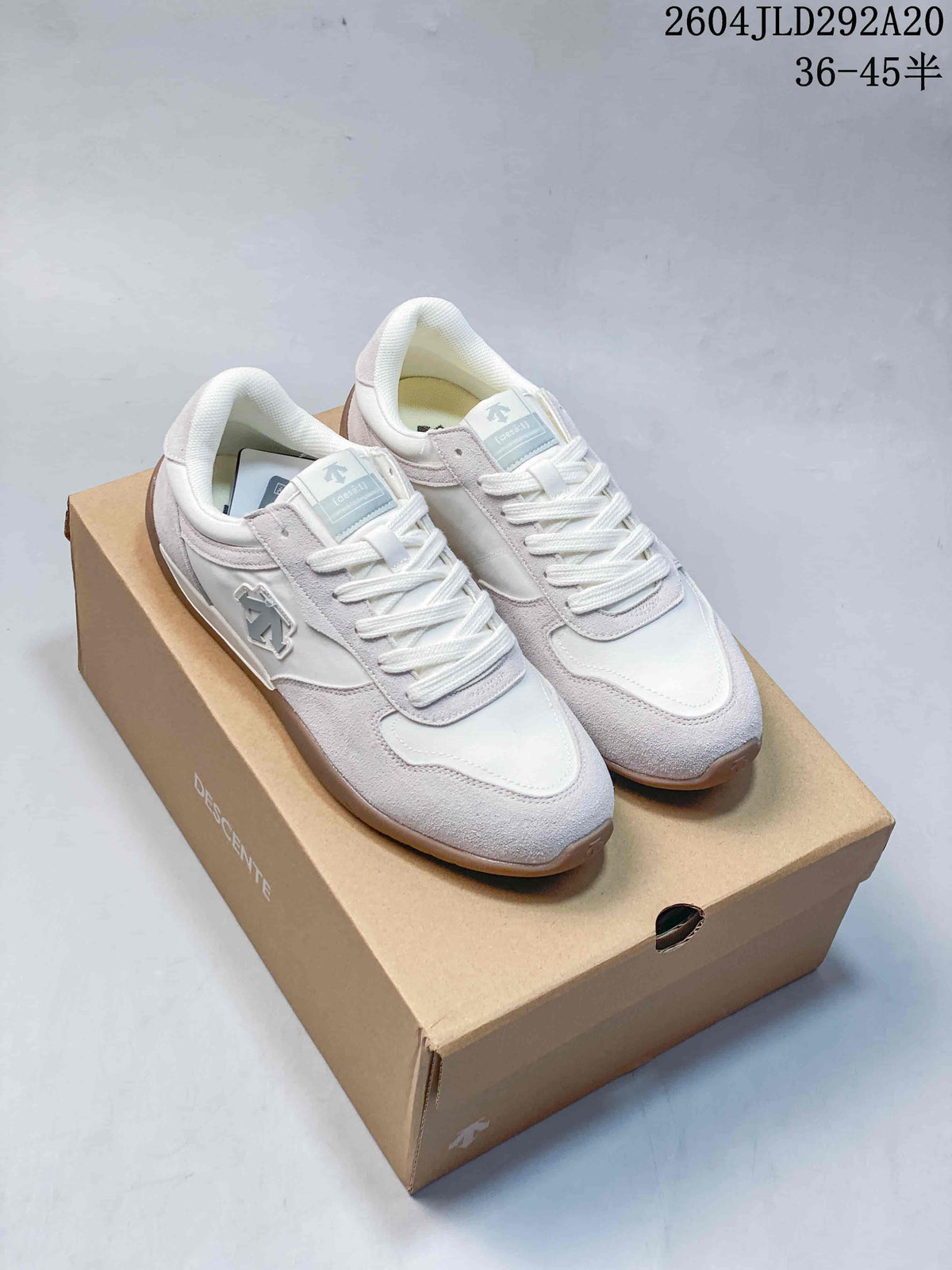 Pair of light-colored DESCENTE CHRON TEMPO Slim low-top sneakers on a branded box; image text shows model code 2604JLD292A20 and a size range.