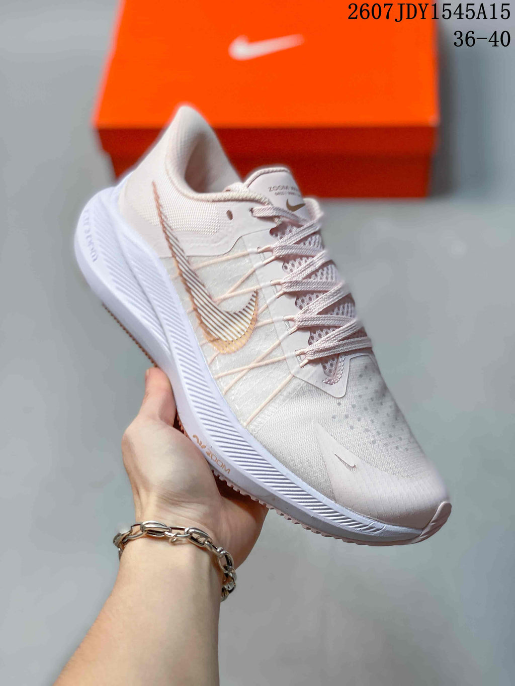 Angled side view of the sneaker showing the pale pink upper, side branding, lace-up construction, and patterned outsole.