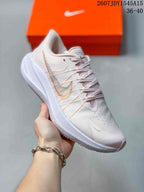 Angled side view of the sneaker showing the pale pink upper, side branding, lace-up construction, and patterned outsole.