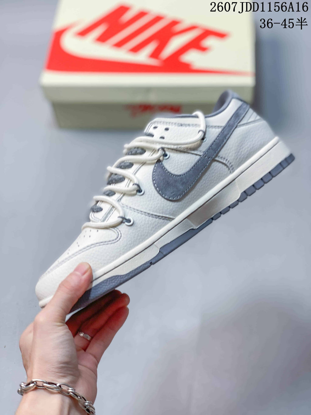 Side profile of an off-white and gray Nike SB Dunk Low sneaker with a gray Swoosh and layered upper panels; image text shows style code 2607JDD1156A16 and size range 36–45.5.