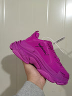 Close-up side view of a vivid purple Balenciaga sneaker showing layered panels, textured sole sections, and repeated branding.