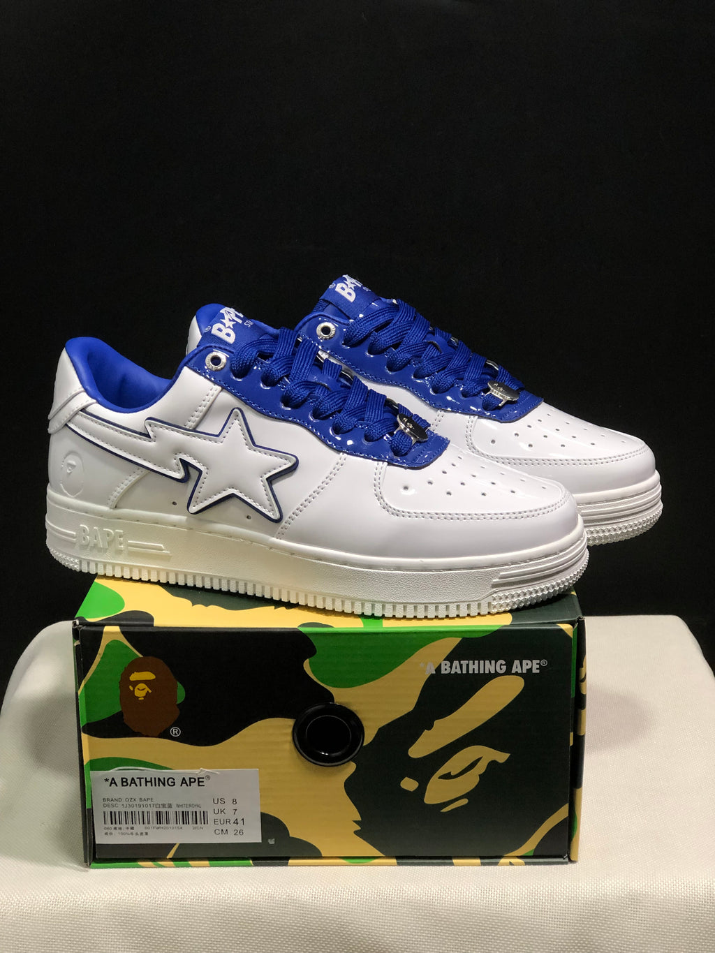 Pair of white and blue BAPE STA low-top sneakers displayed on a patterned BAPE shoebox; the box label shows EU 41, UK 7, US 8, and CM 26.