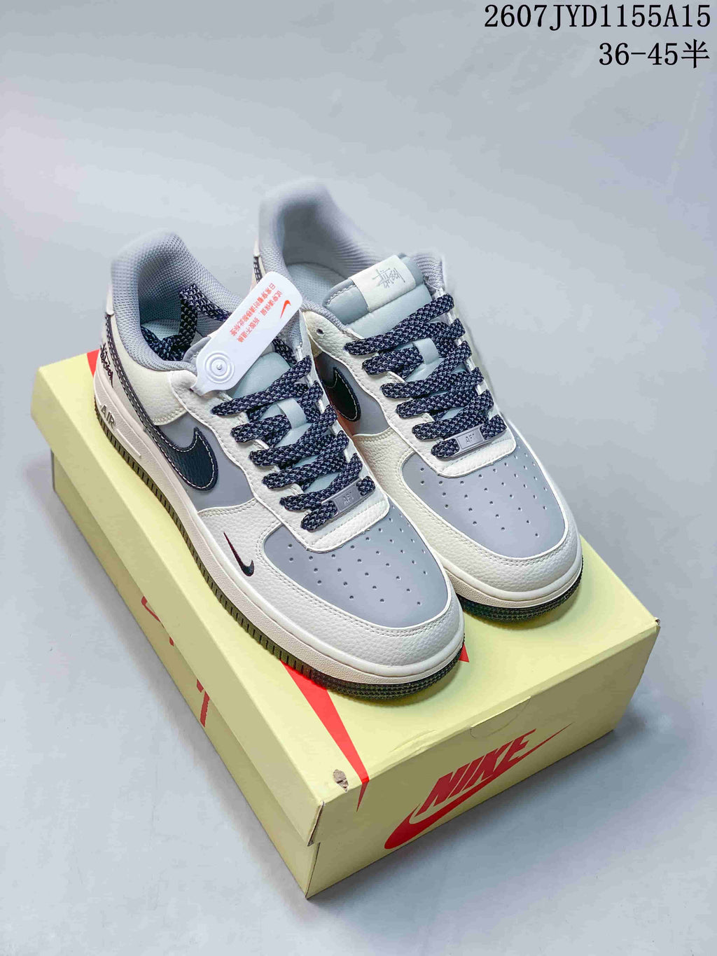 Pair of grey, white and navy Nike Air Force 1 sneakers displayed on a Nike shoebox, with style code 2607JYD1155A15 and size range 36–45.5 shown in the image.