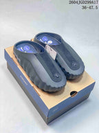 Pair of black and dark gray Nike Mind 001 slides displayed on a presentation box; the image shows the printed range 36–47.5.