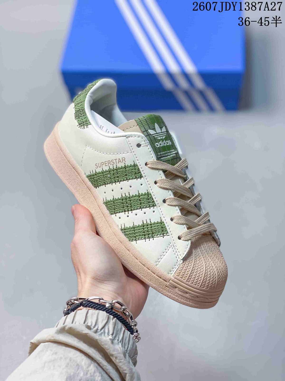 Three-quarter side view showing the Superstar side branding, green striped detailing, beige shell toe, and beige outsole.