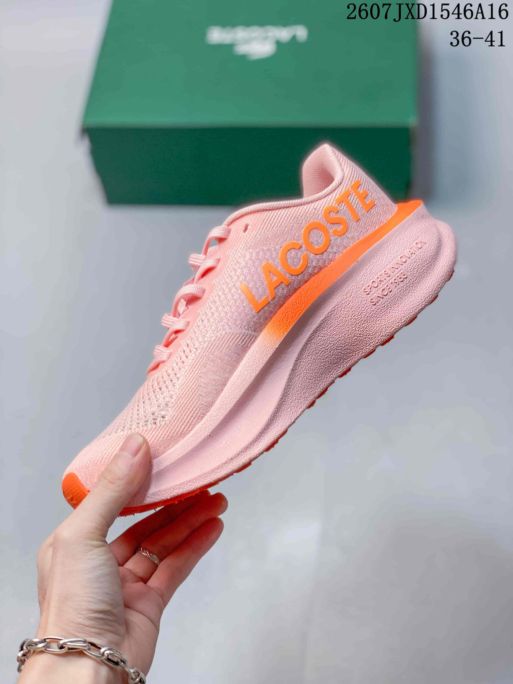 Side profile of the pink low-top sneaker with orange side branding and a Lacoste emblem.