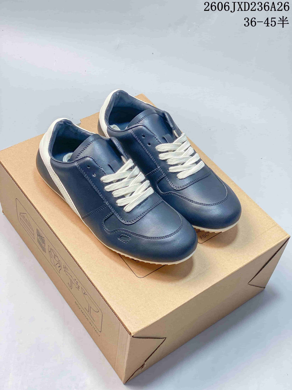 Navy low-top lace-up sneakers with white laces and heel accents, photographed on a box.