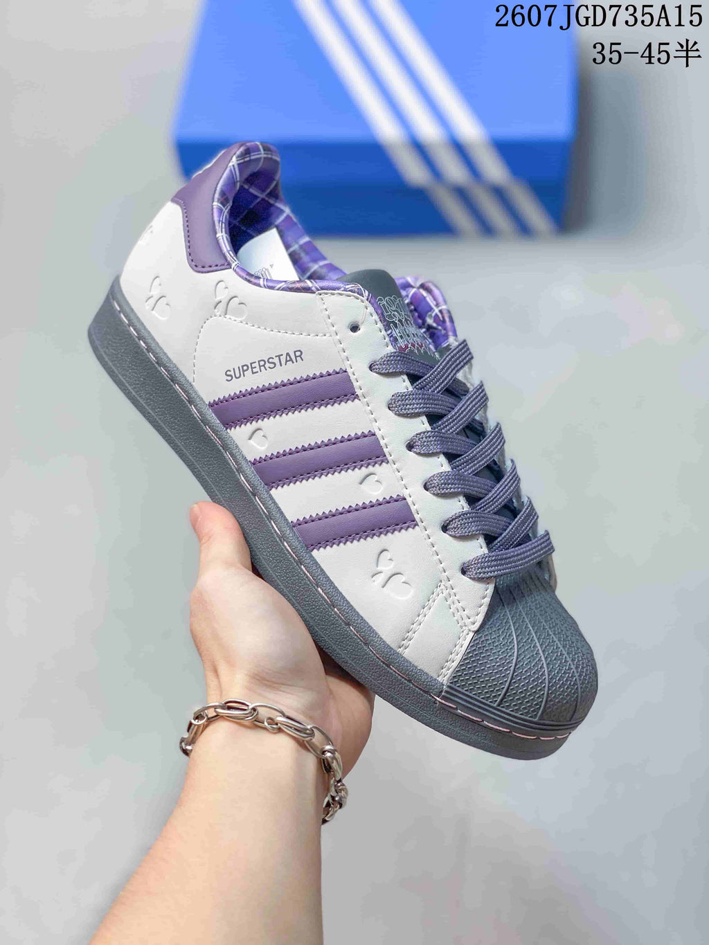 Angled side view showing the white upper, purple stripes, gray shell toe, gray outsole and Superstar side branding.