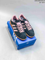 Pair of black and pink Adidas Originals Gazelle Indoor sneakers displayed on a blue Adidas shoebox.