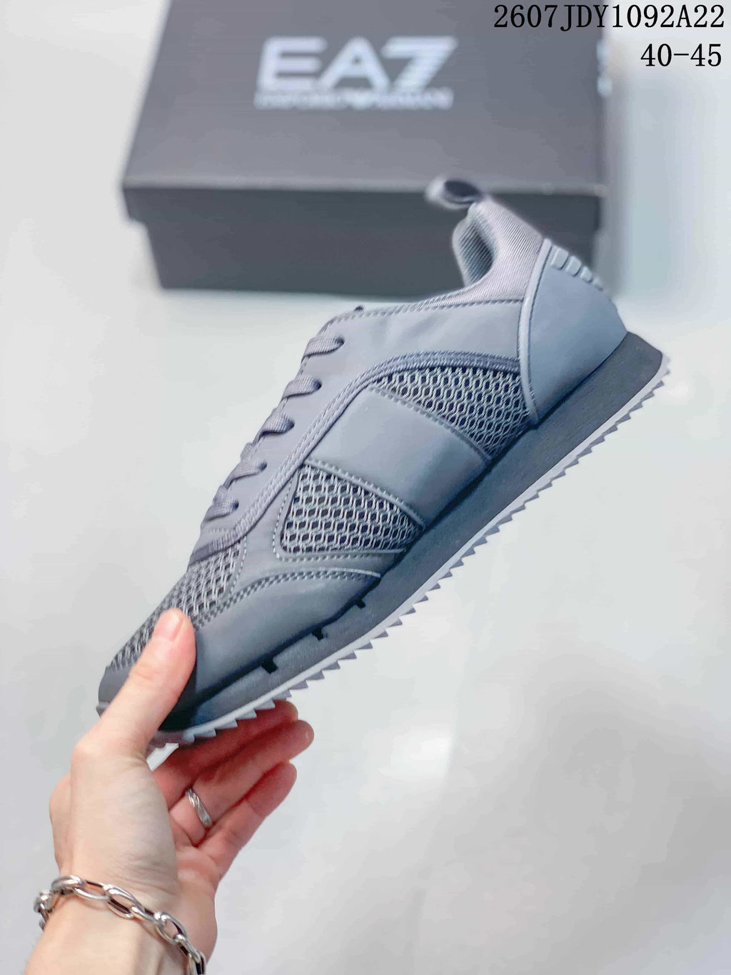 Side view of the gray sneaker showing mesh panels, tonal overlays, lace-up construction, and a ridged outsole.