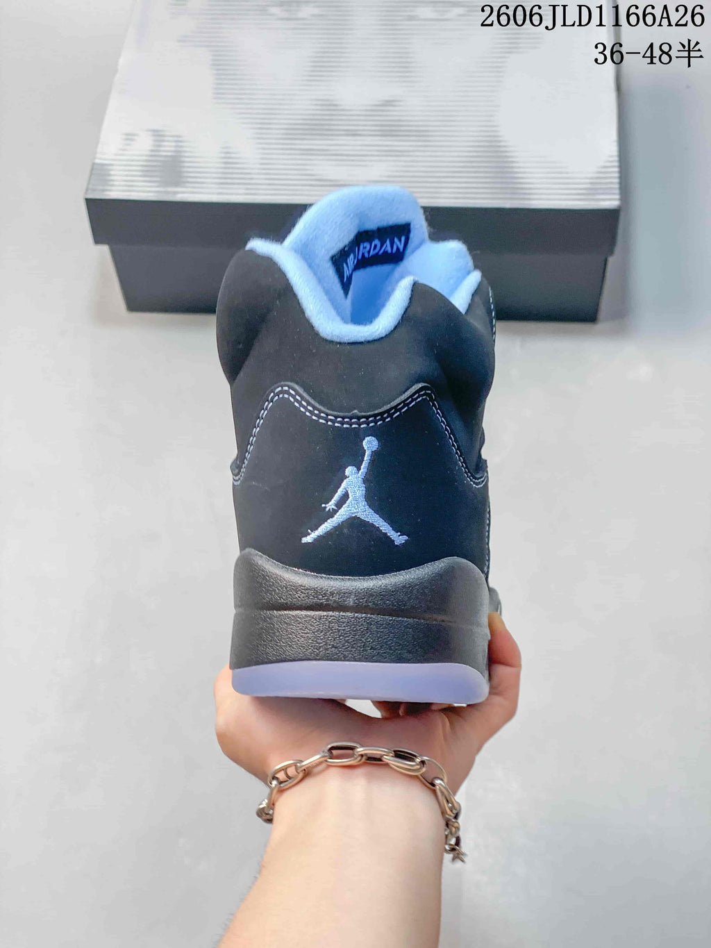 Rear view of a dark high-top sneaker with a Jumpman-style heel emblem and light blue collar lining.