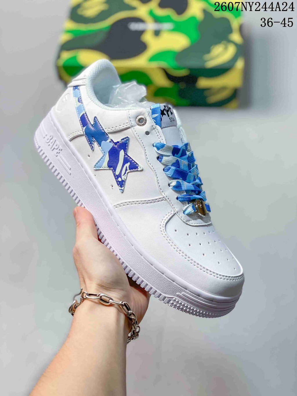 White low-top sneaker with blue star graphic, blue-and-white laces and white sole; source overlay shows style code 2607NY244A24 and size range 36–45.