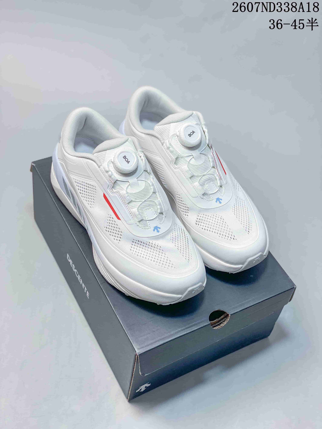 Pair of white Descente D.F. Wire 3.0 sneakers displayed on a black shoebox, showing the BOA dials, perforated upper and red accents.