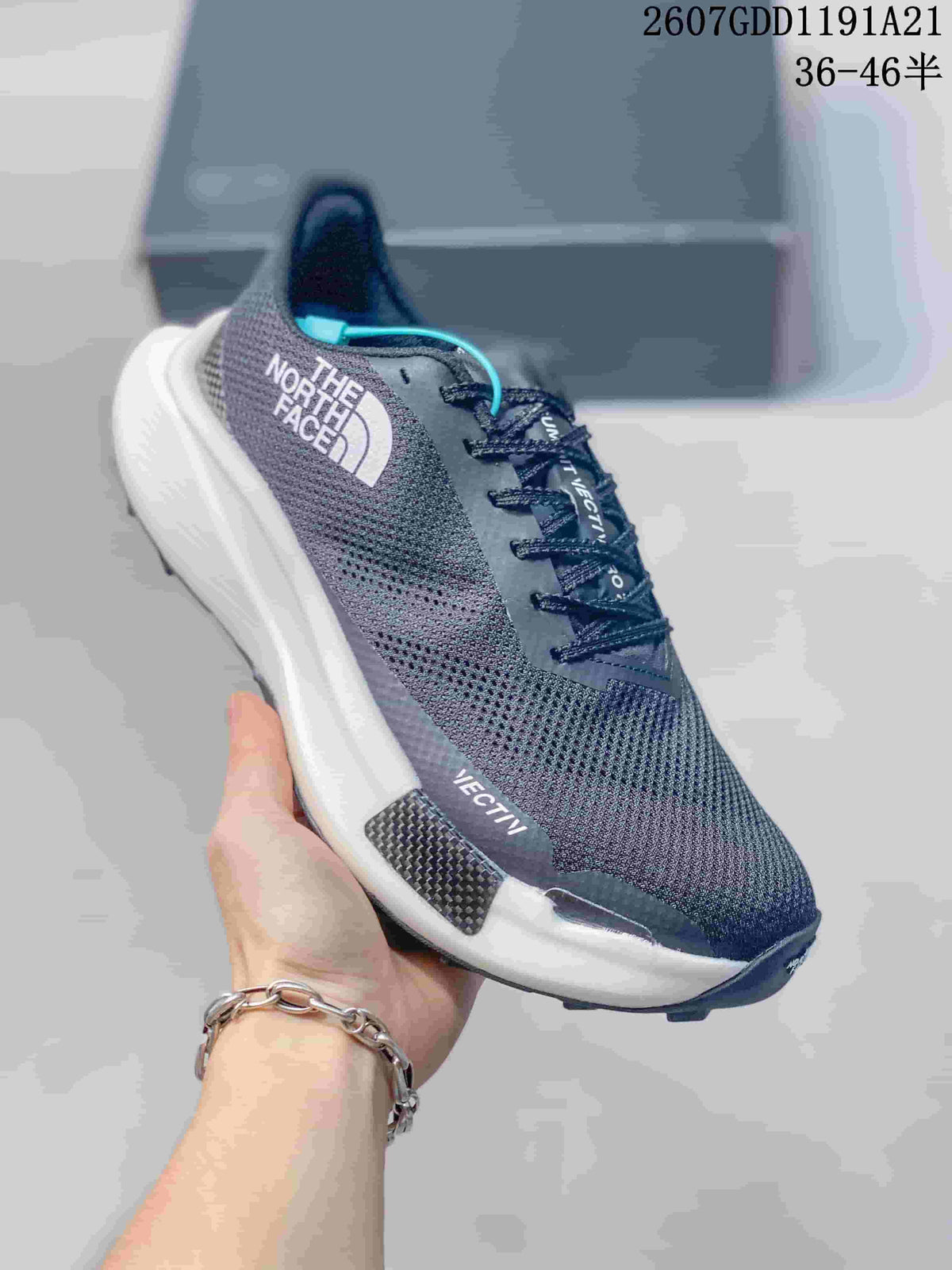 Angled side view of the dark gray sneaker showing the The North Face logo, mesh upper, white midsole, and lugged outsole.