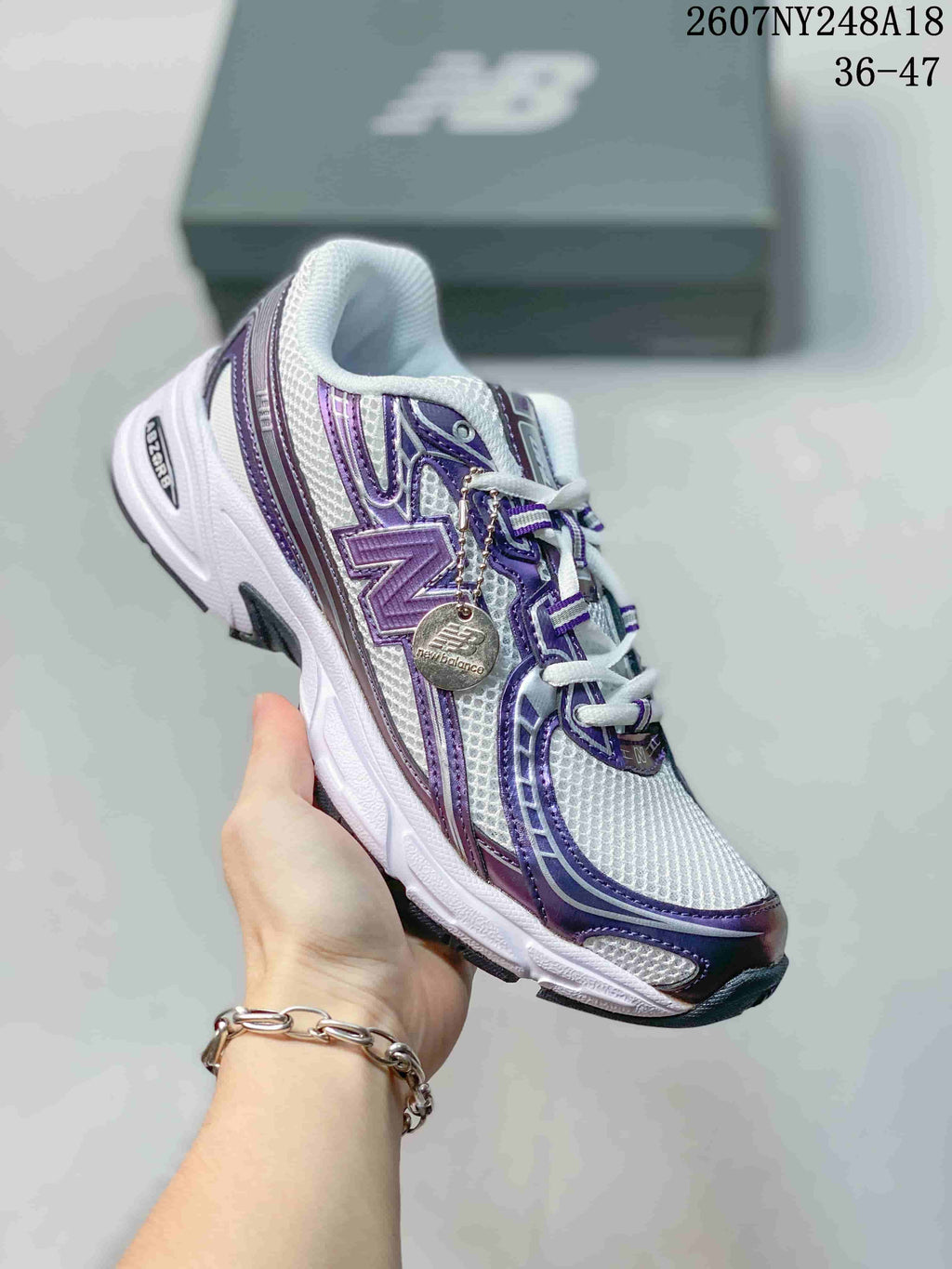 Angled side view of the white and purple New Balance 740 sneaker with visible branding and attached decorative tag.
