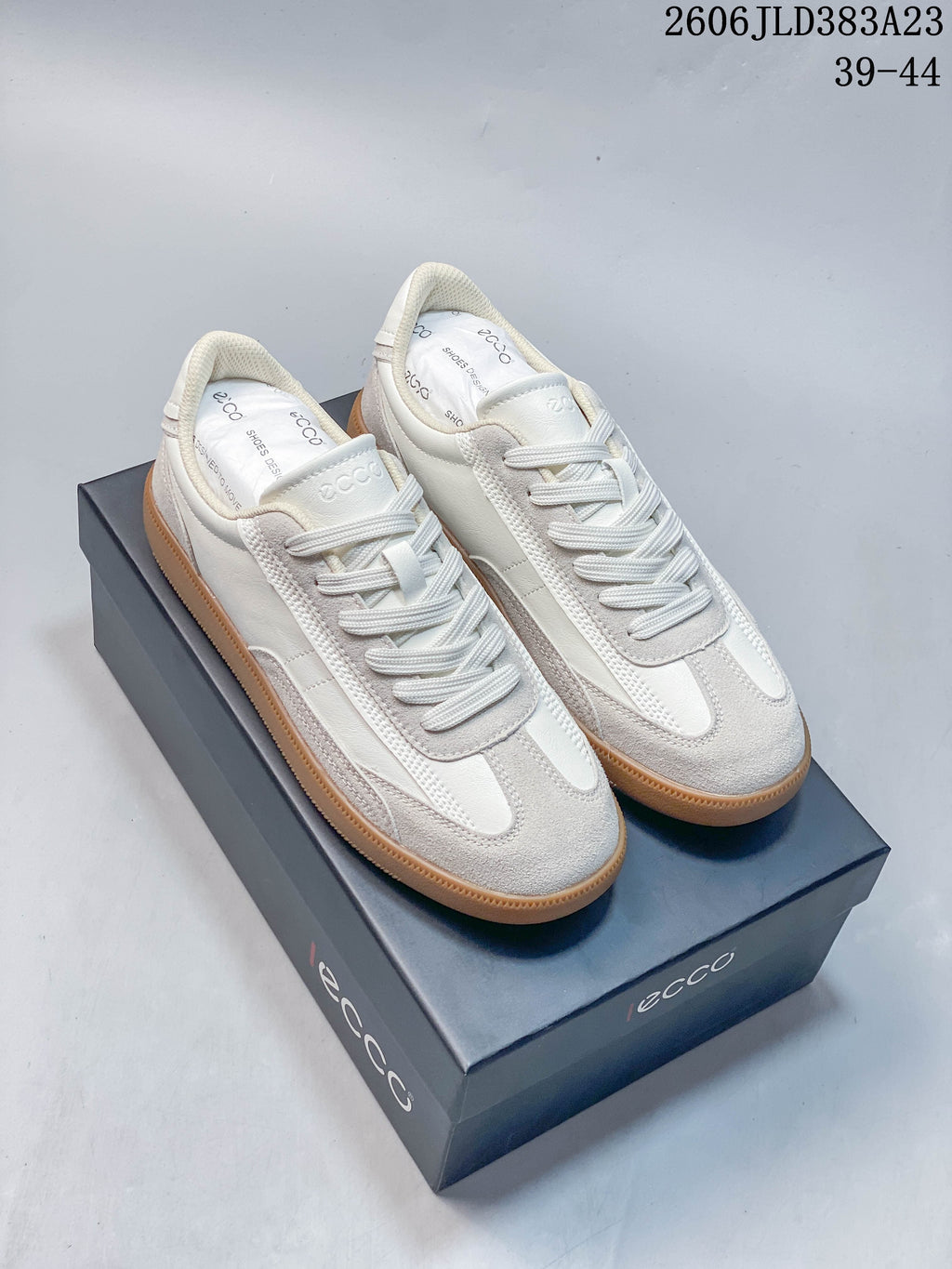 Pair of off-white ECCO low-top sneakers with textured overlays and gum-colored soles, displayed on a branded box; image overlay shows sizes 39–44 and code 2606 JLD383A23.