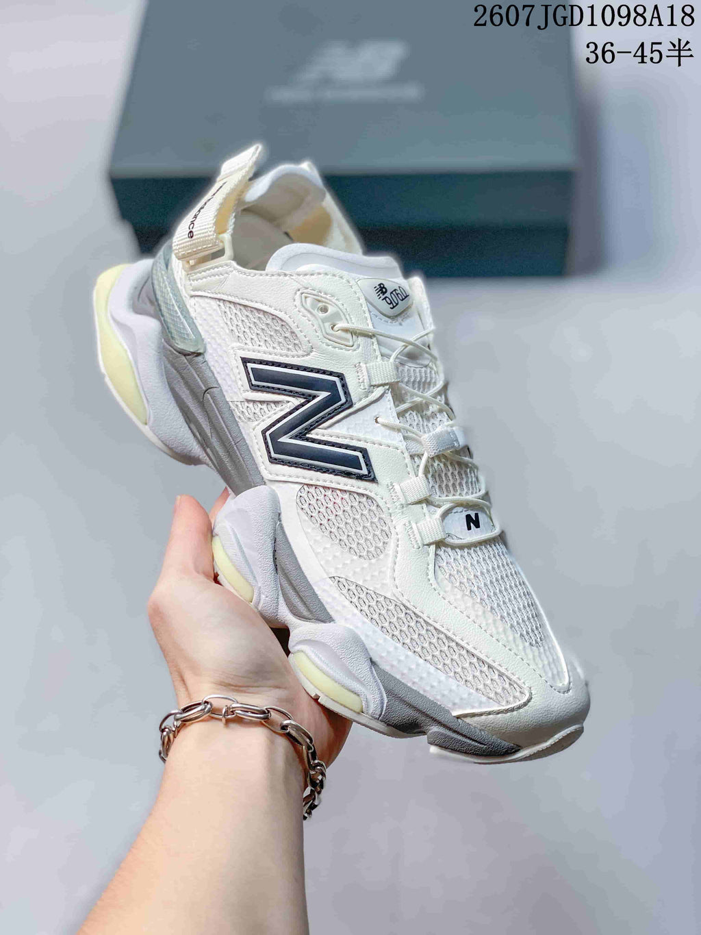 Angled side view of a white and light grey New Balance 9060 sneaker with a large contrast N logo, mesh upper and pale yellow outsole accents.