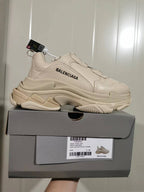 Beige Balenciaga Triple S sneaker displayed on its box, showing the side branding, chunky layered sole, and box label.