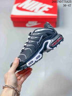Side profile of the black and white Nike Air Max Plus TN sneaker showing layered panels, white accents, and visible midsole cushioning windows.