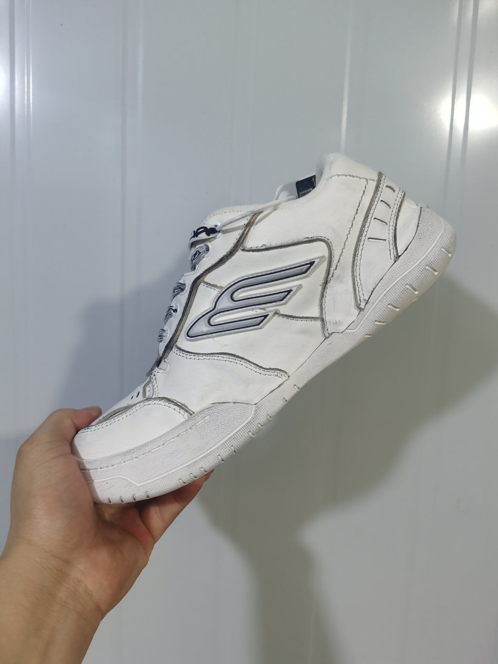Side view of a white Balenciaga sneaker showing the outlined side logo, layered upper panels, laces, and textured sole.