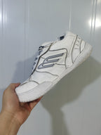 Side view of a white Balenciaga sneaker showing the outlined side logo, layered upper panels, laces, and textured sole.