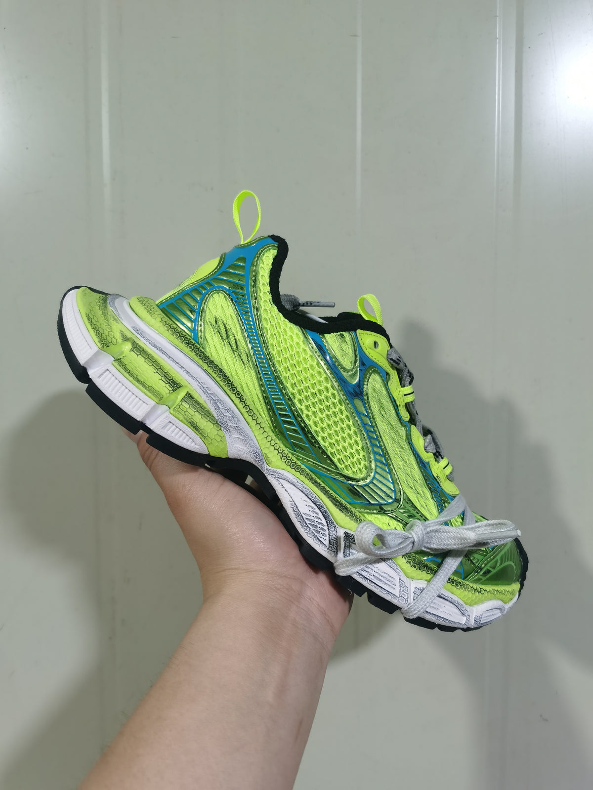Angled view showing the fluorescent yellow and blue sneaker upper, blue structural overlays, gray laces, and black outsole.