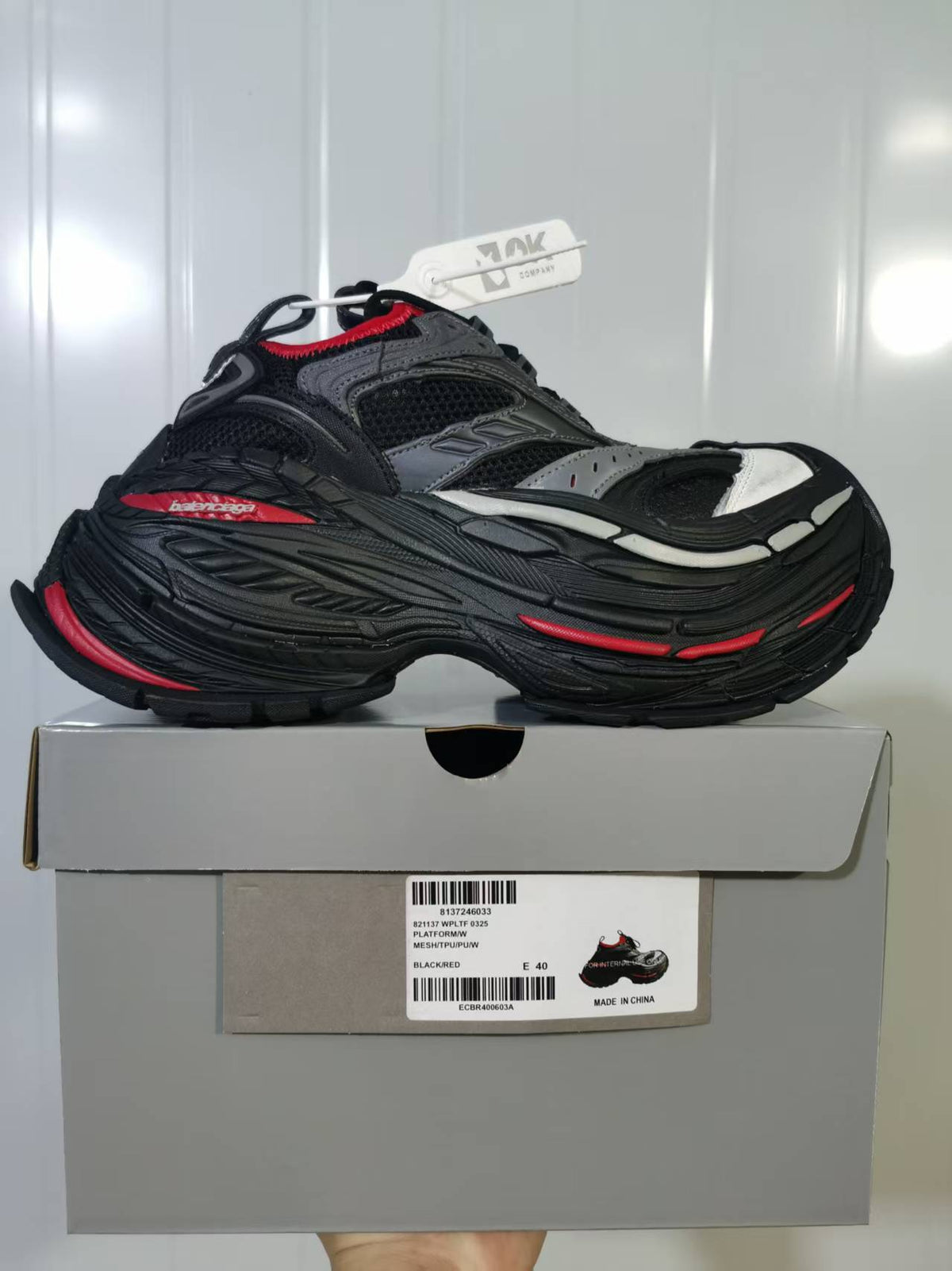 Side view of the black and red sneaker placed on its box; the label shows model reference 0325, black/red color, and a photographed size of E 40.