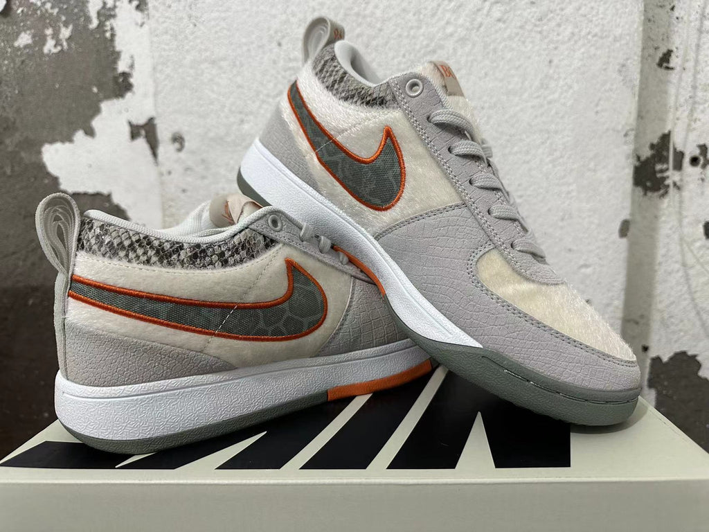 Pair of gray and off-white Nike Book 1 sneakers with orange accents, shown from the side.