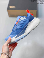 Side profile showing the blue mesh-style upper, layered overlays, orange details, and lugged outsole.
