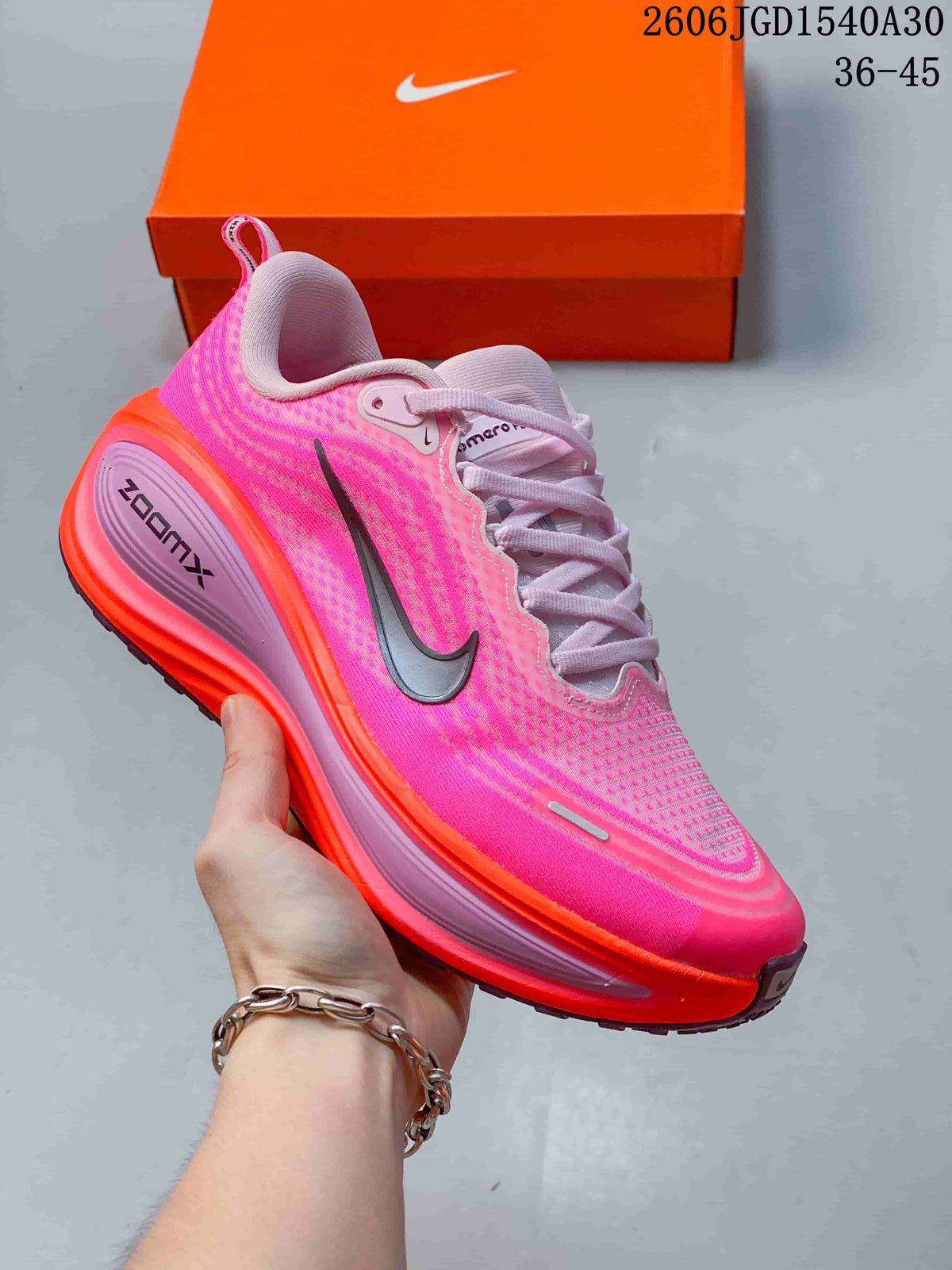Pink Nike Vomero Plus running shoe with orange accents and a sculpted-looking sole.