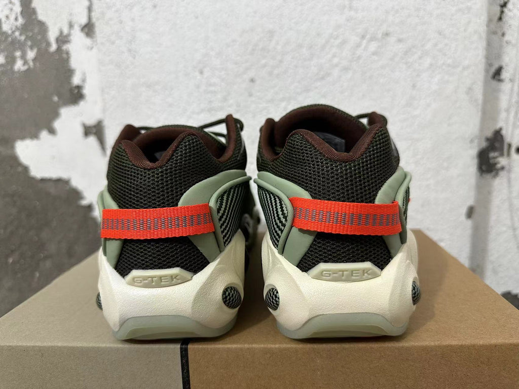 Rear view of dark mesh sneakers with green-toned overlays, cream-colored soles, and orange heel straps.