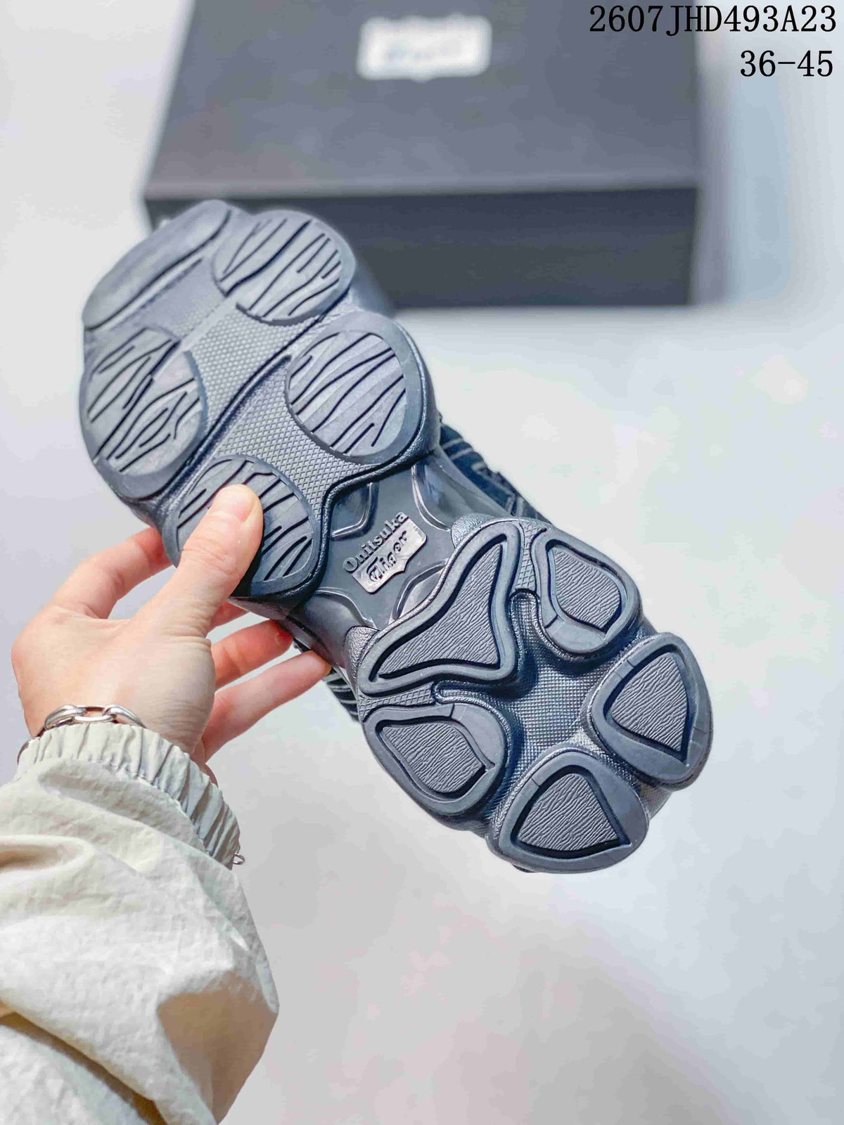 Underside of a dark Onitsuka Tiger sneaker showing the segmented sculpted outsole tread.