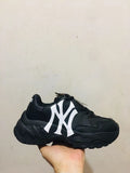 Black chunky low-top sneaker with a large white interlocking side logo, black laces, and a textured outsole.