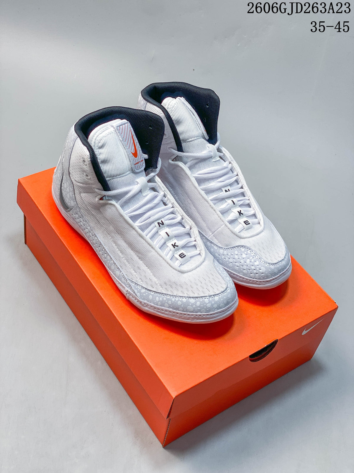 Pair of white and grey Nike Inflict 4 wrestling shoes on an orange shoebox