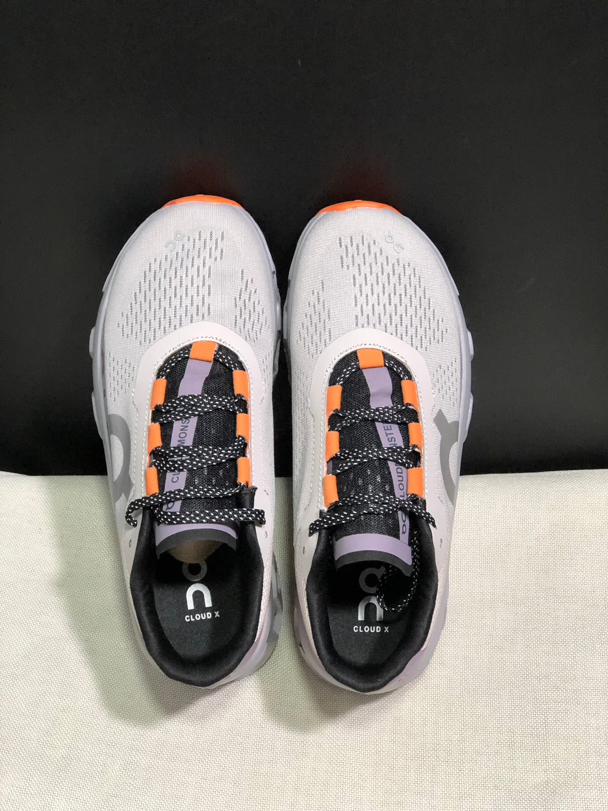Top view of the gray On Cloud X pair with patterned black laces and orange lace-loop accents.