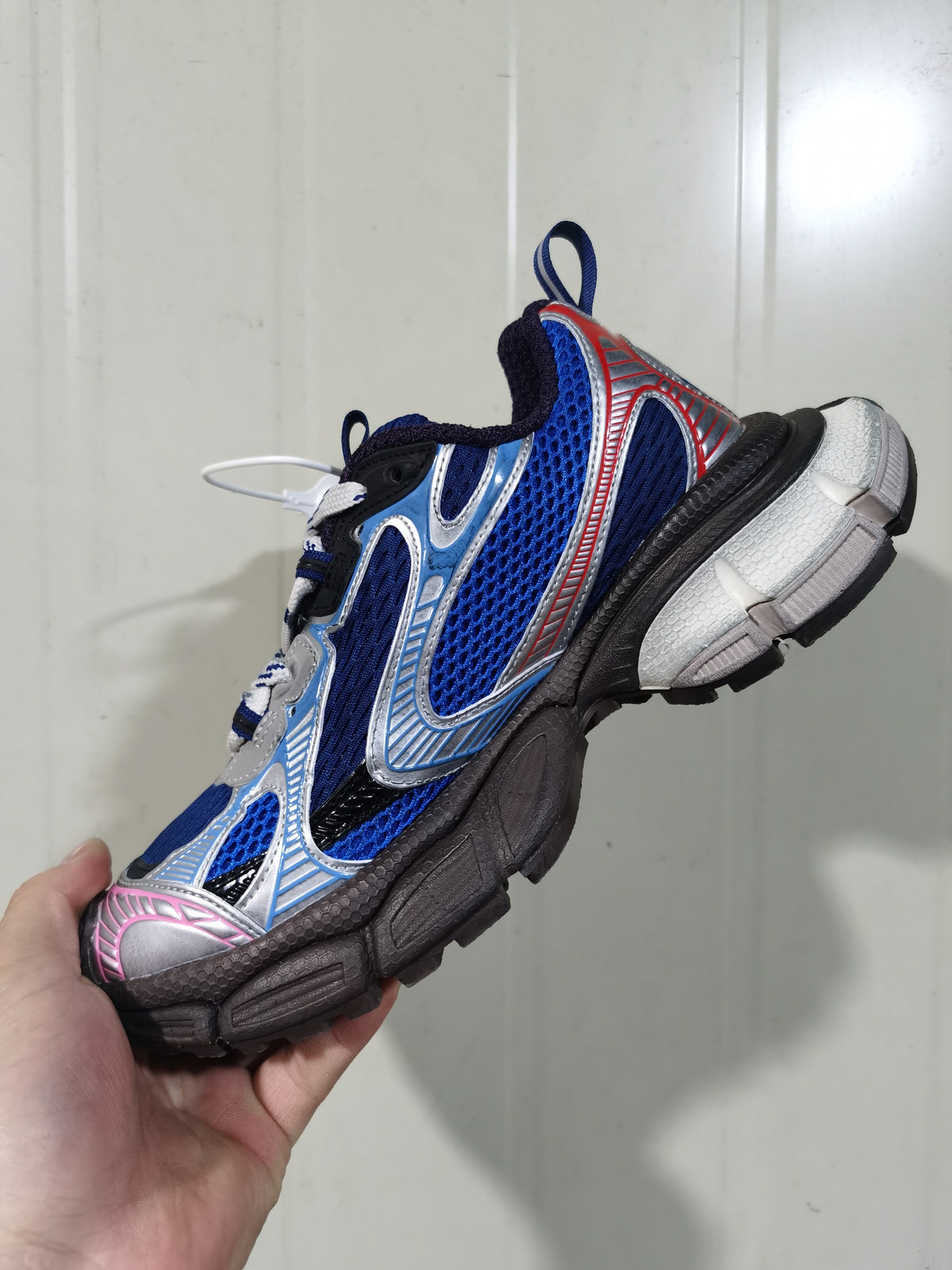 Side and sole view of the sneaker showing blue mesh-style panels, silver overlays, pink toe detailing, and a textured black outsole.