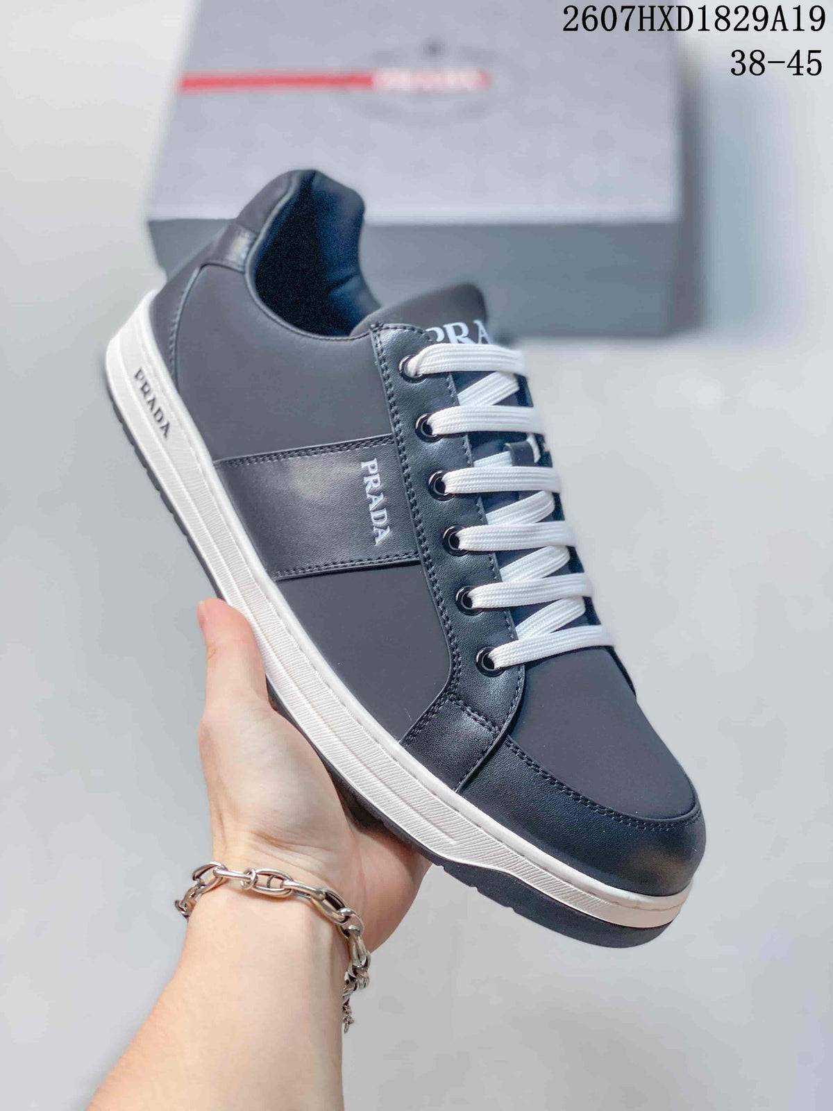 Side view of a navy Prada Downtown low-top sneaker showing the lace-up front, branded side panel and contrasting sole; style code 2607HXD1829A19 and size range 38–45 are visible.