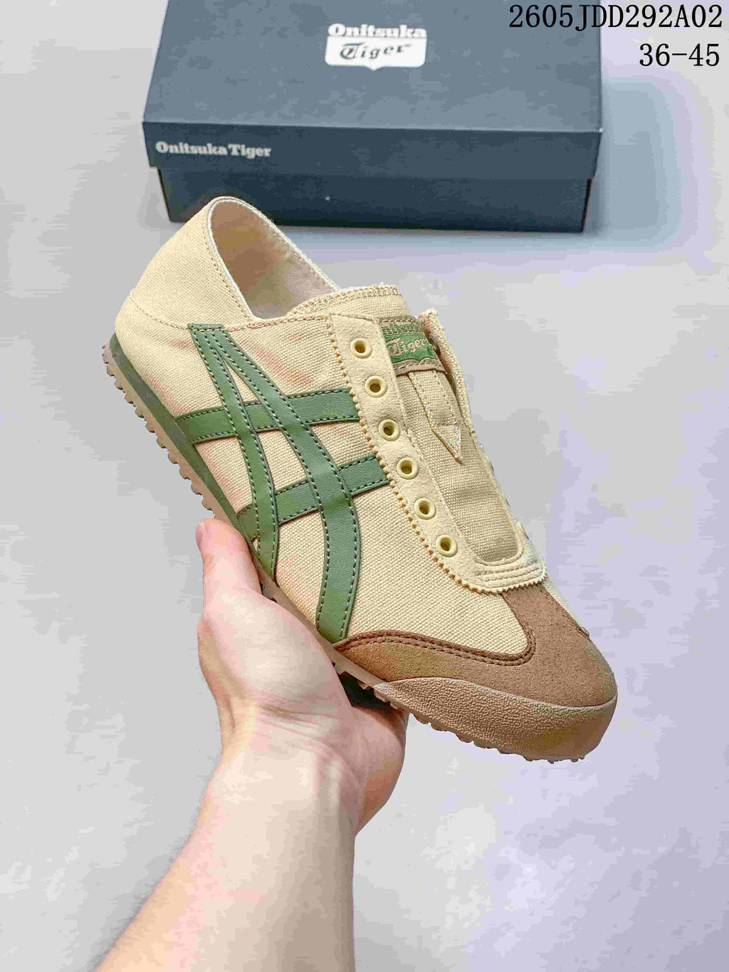 Angled close-up of the beige Onitsuka Tiger Mexico 66 slip-on sneaker showing green side stripes, brown toe overlays, and the textured outsole.