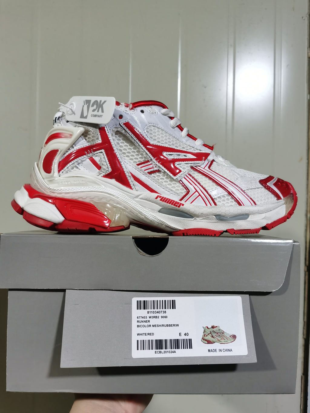 White and red ASICS sneaker displayed on its box; the label identifies WHITE/RED, size E 40, and RUNNER MESH/RUBBER/W.