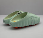 Rear three-quarter view showing the open heel, heel branding, interior footbed, and orange outsole details.