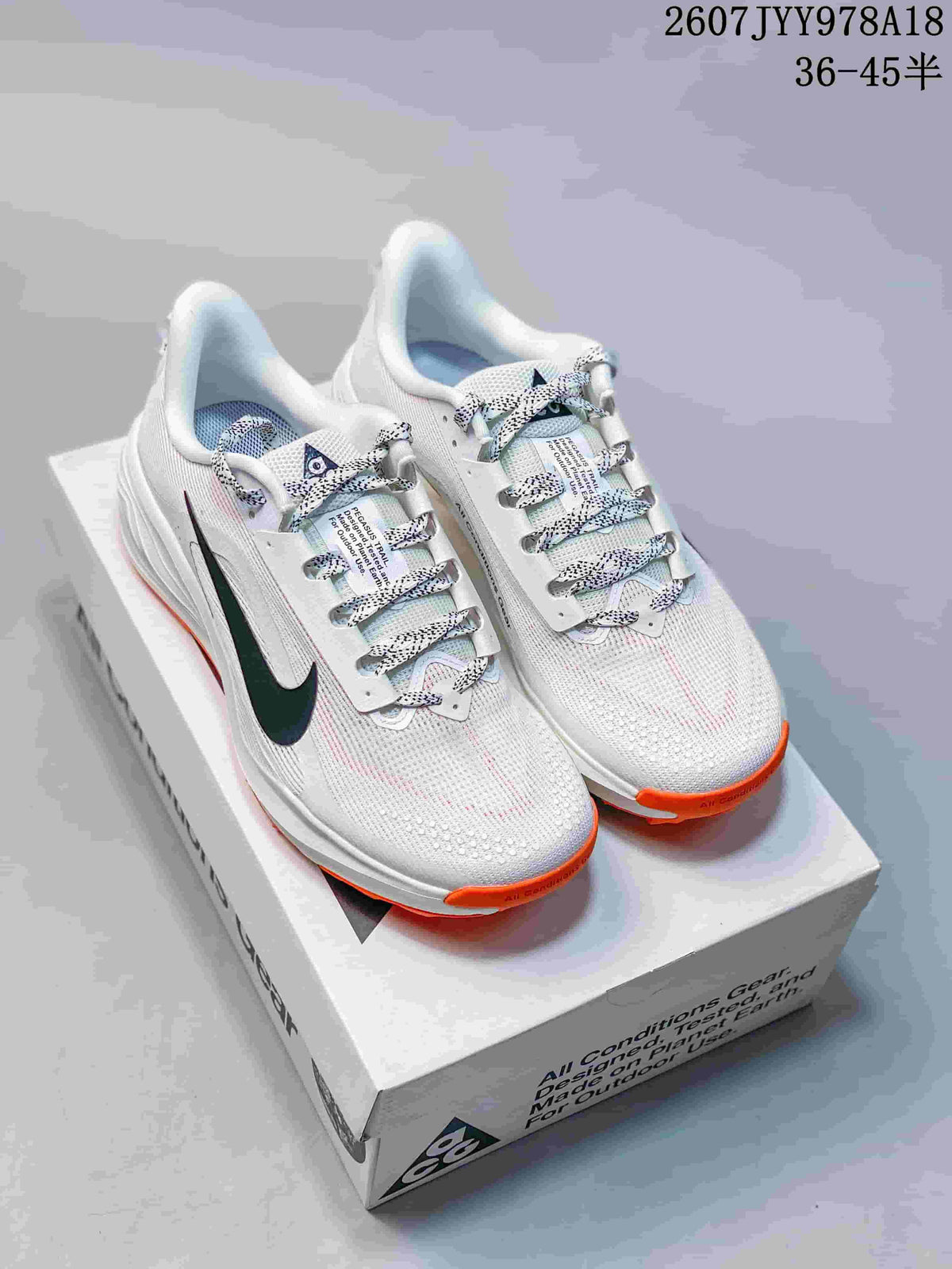Pair of Nike ACG Pegasus Trail shoes in a light colorway with dark Swoosh branding and orange outsole accents, displayed on an ACG shoebox.