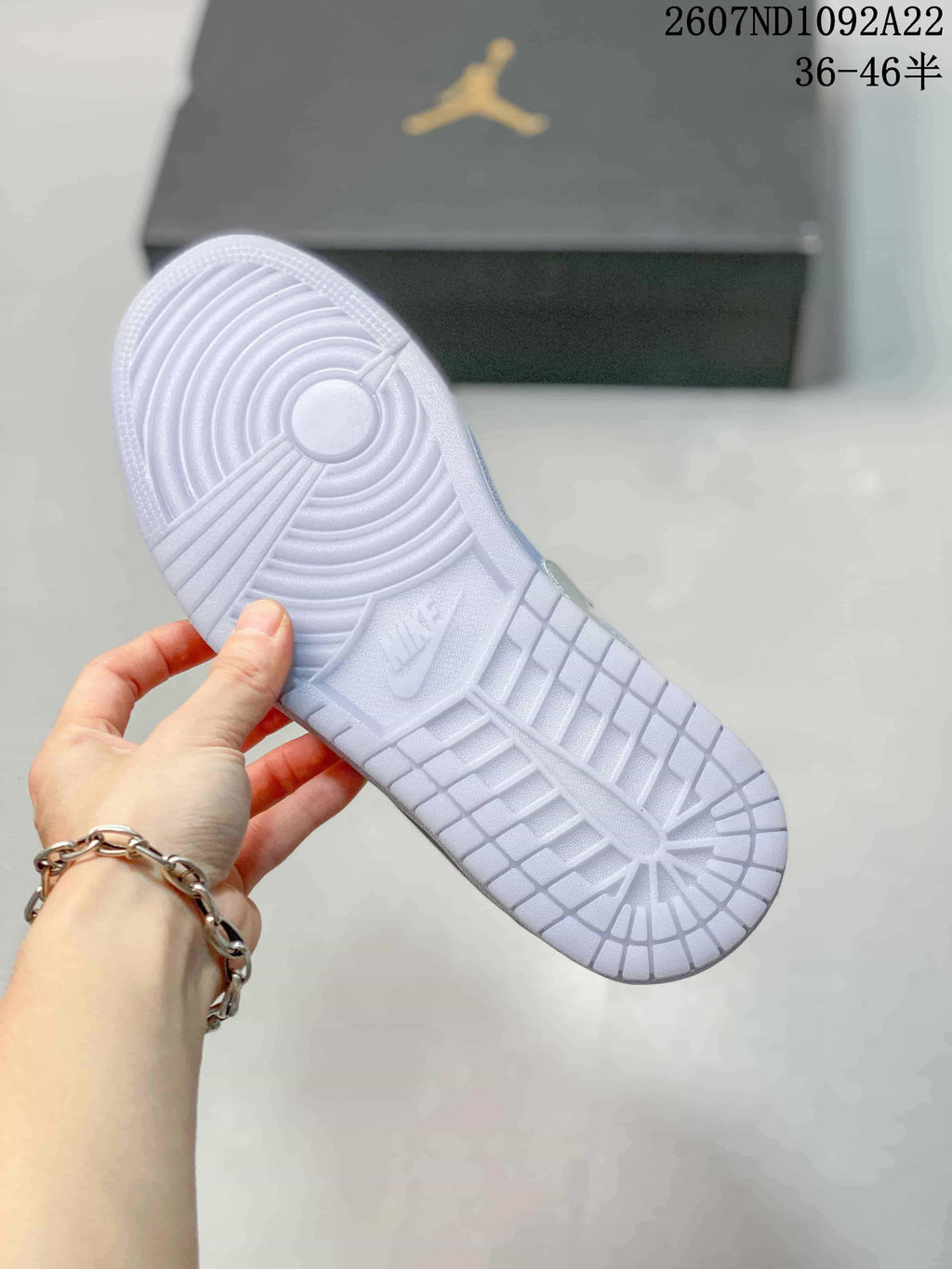 Underside of a light-colored sneaker showing a circular rubber outsole pattern and embossed branding.