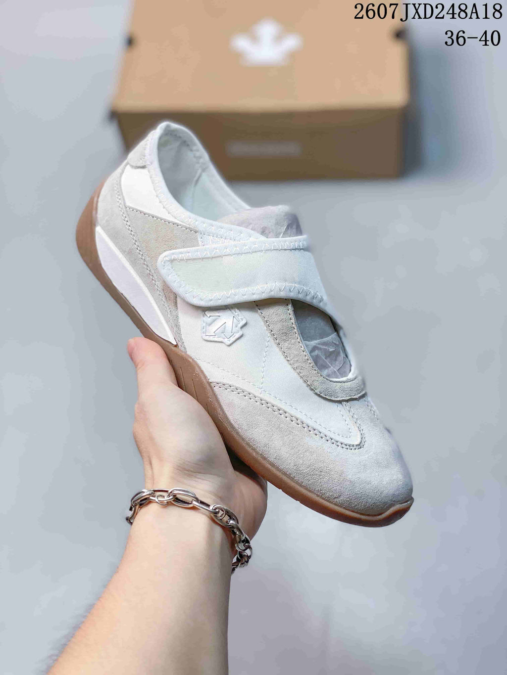 Close side view of a white sneaker with a wide strap, embroidered side emblem, and gum-style outsole.