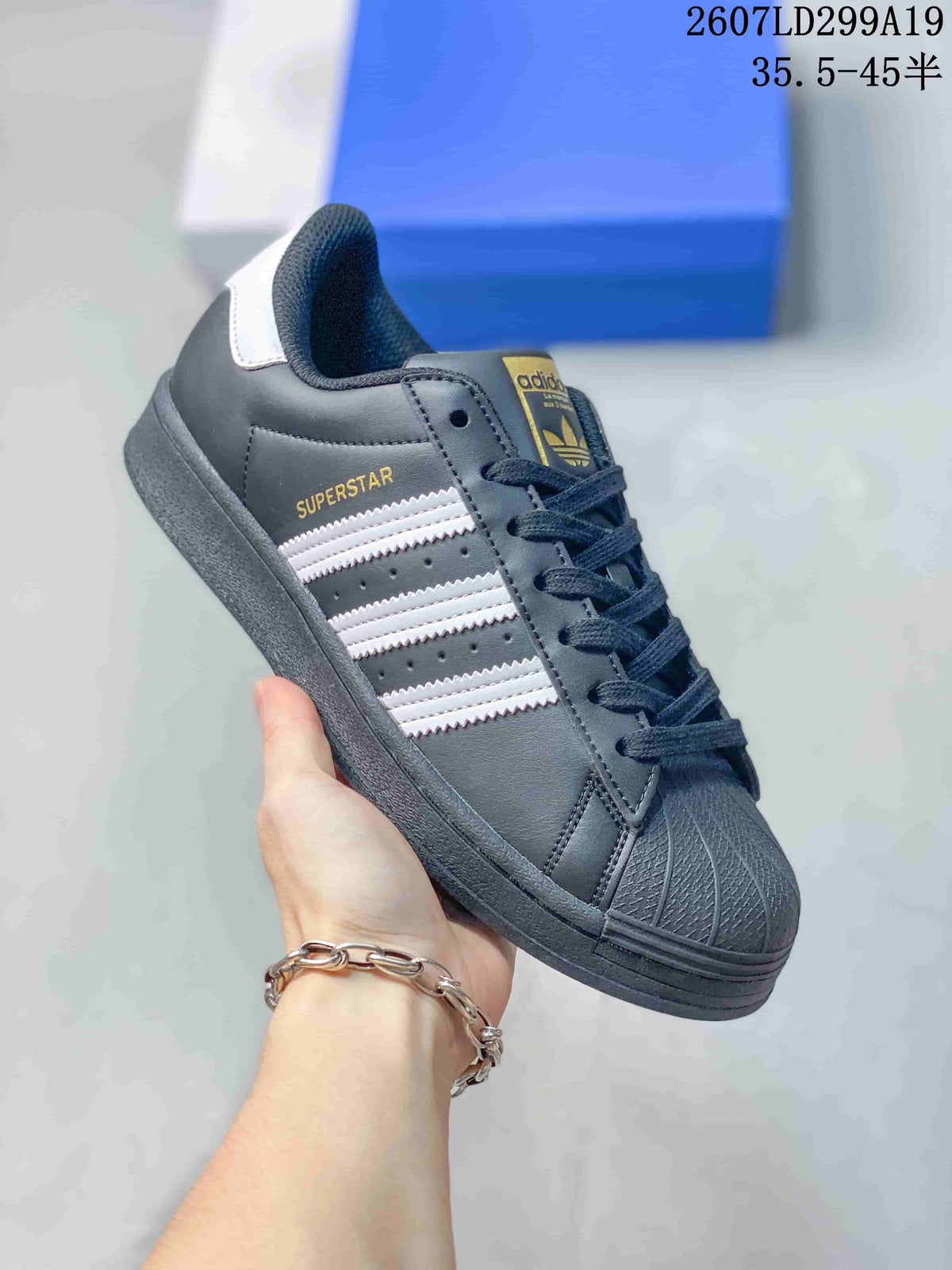 Angled side view showing the black upper, white stripes, gold Superstar branding, and white heel tab.